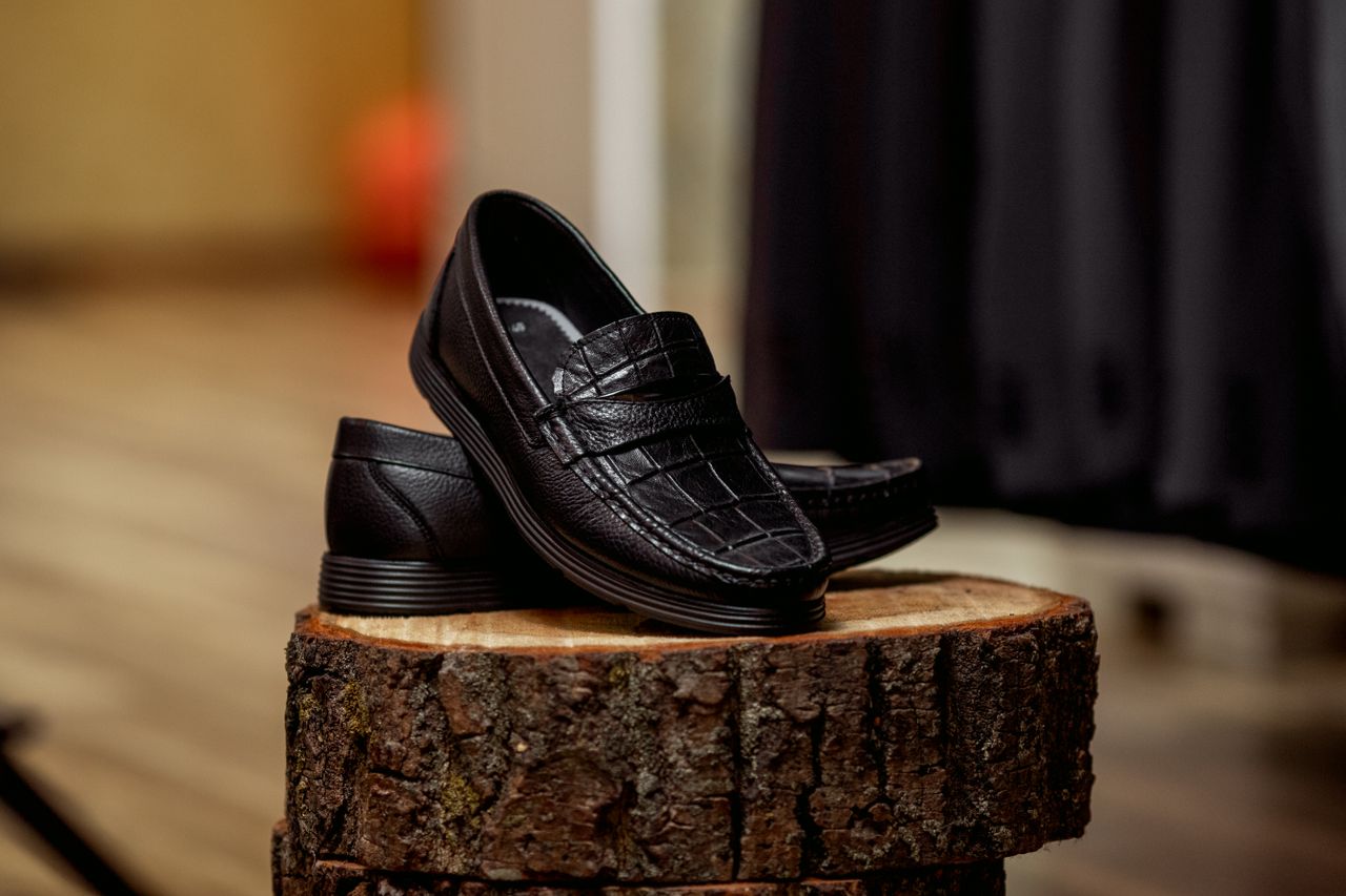 team-01 Stylish black loafers displayed on wood, highlighting detailed craftsmanship.